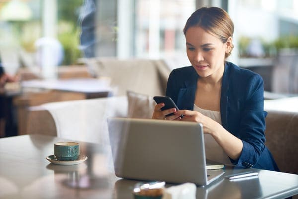 woman distracted on her cellphone sitting in front of her laptop