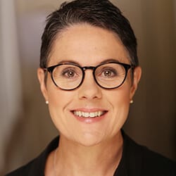 Tracy Sinclair MCC headshot photo, smiling woman wearing glasses and a black blazer in front of neutral background
