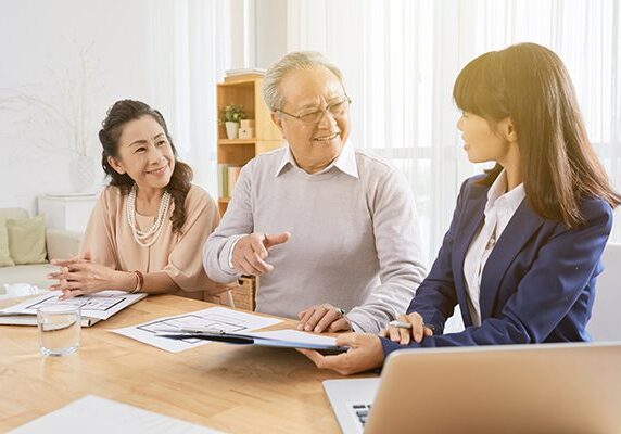 two older people sitting next to a younger coach who is showing them something on some paper and a laptop