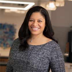 Anitra St Hilaire headshot photo, dark haired woman wearing a gray top smiling with blurred office background