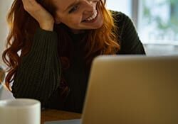 woman smiling looking at a laptop screen at a table