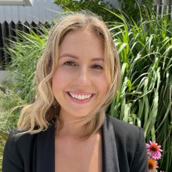 Julia Telford headshot photo, blond woman smiling outside in a garden wearing a black blazer
