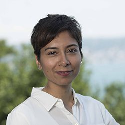 Uzma Mohamedali PCC headshot photo, smiling woman with short brown hair and white shirt standing outside