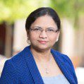 Vatsala Sarathy headshot photo, dark haired woman smiling in blue blazer outside