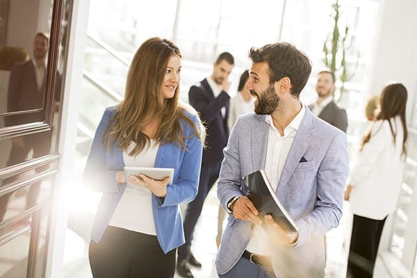 two professionals engaging in conversation and walking in a busy hall way
