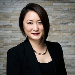 Michelle Wu ACC headshot photo, smiling woman with dark hair wearing dark blazer and top in front of brick wall