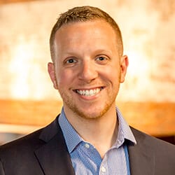 Adam Yosim headshot photo, smiling man in dark suit with light collared shirt in front of orange background