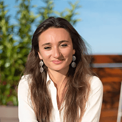 Nour Ashari ACC headshot photo, dark haired woman smiling in a white top outside